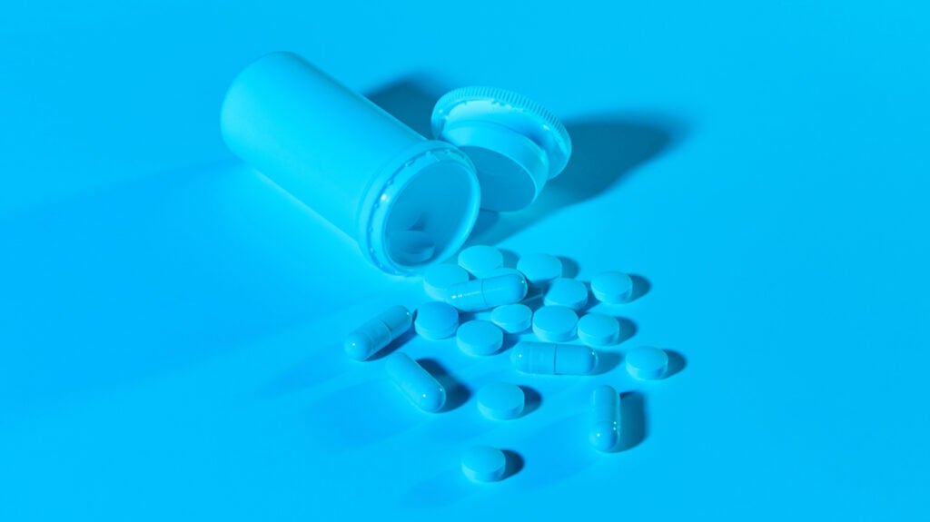 A pillbox with pills spilling out under blue lighting