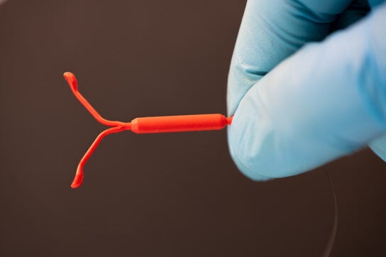 A hand in a medical glove holding an intrauterine device