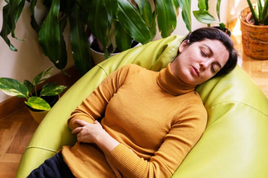 An image of someone laying down, with their eyes closed, and arms around their stomach.