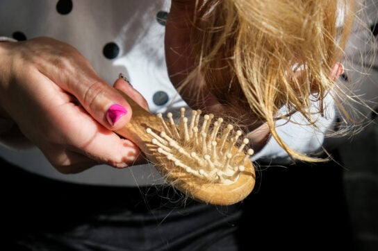 Close up of someone bending forward brishing their hair with lots of hair attached to their hairbrush depicting medications that cause hair loss
